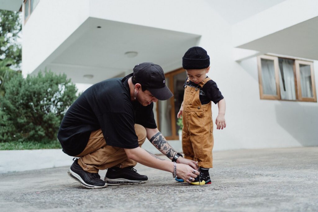 A father helps his young son tie his shoelace outdoors, showcasing family bonding.