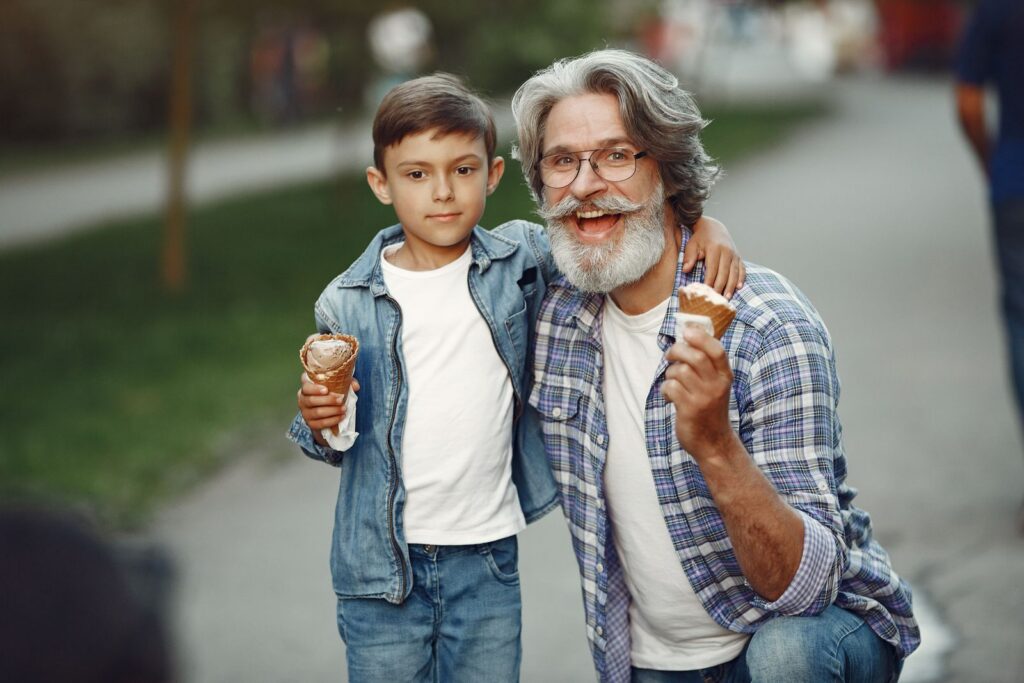 Happy grandfather and grandson sharing ice cream cones together outdoors on a sunny day.