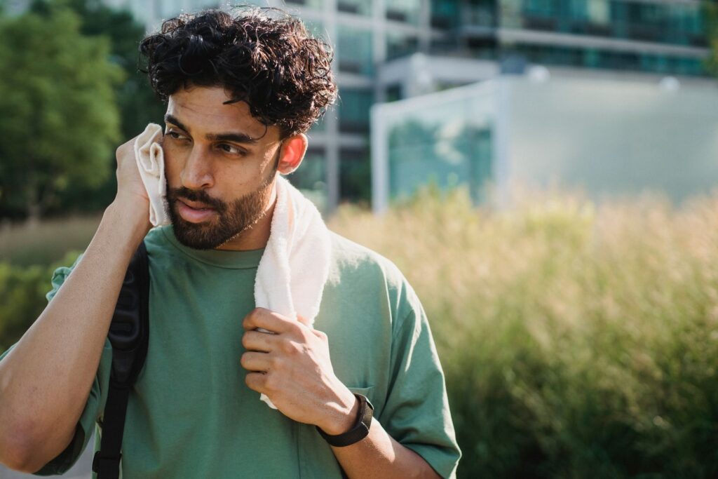 Man taking a break from exercise, using a towel to cool down outdoors on a sunny day.