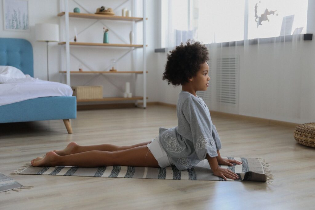 Side view of charming African American girl doing Bhujangasana and warming up on rug in bedroom