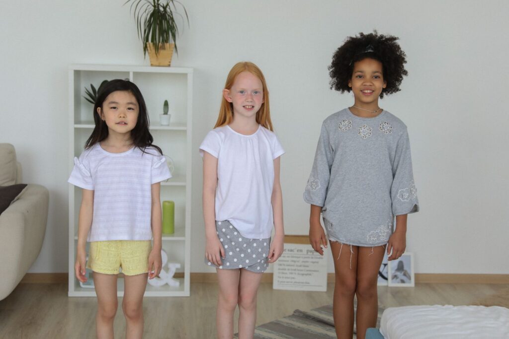 Happy multiracial children in pajamas standing together in living room and looking at camera while smiling