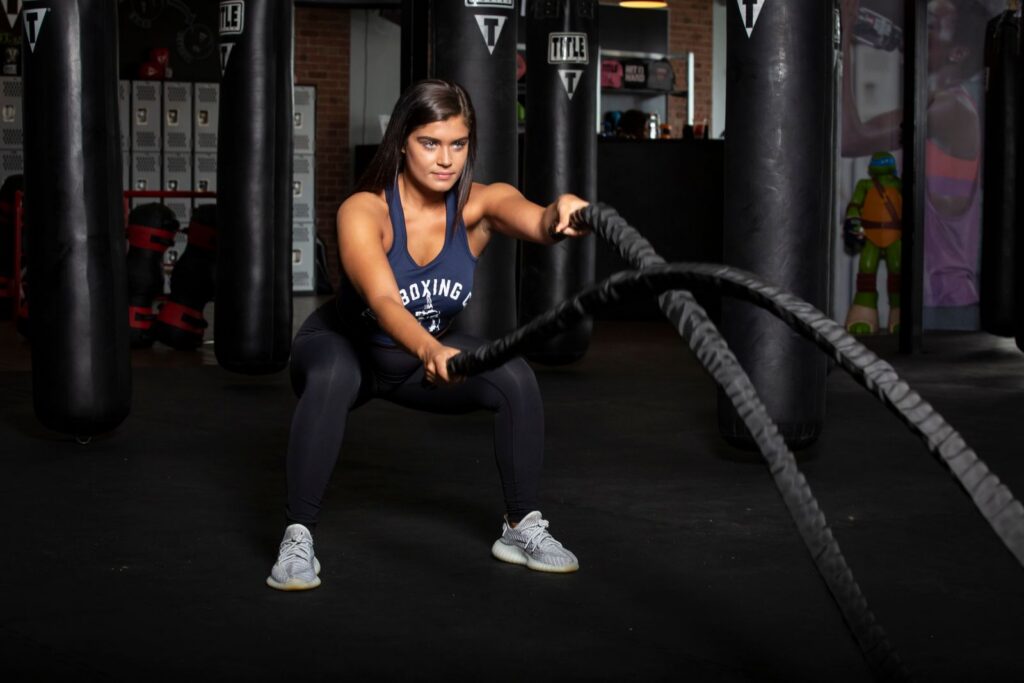 Female athlete working out with battle ropes to release stress.