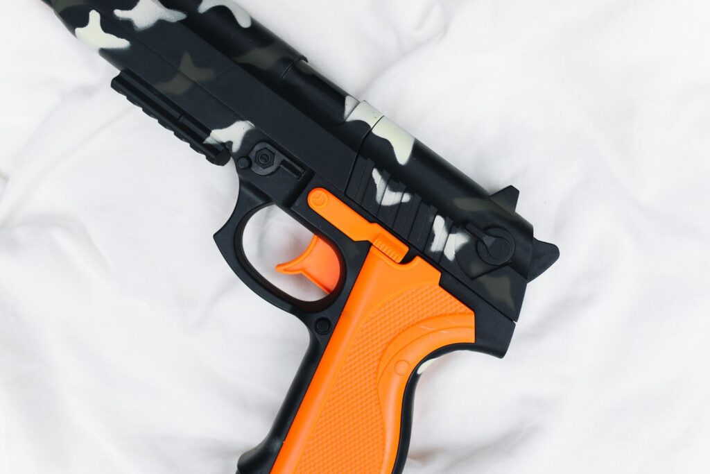 Close-up of a camouflage toy gun with orange features on a soft white fabric, creating contrast.
