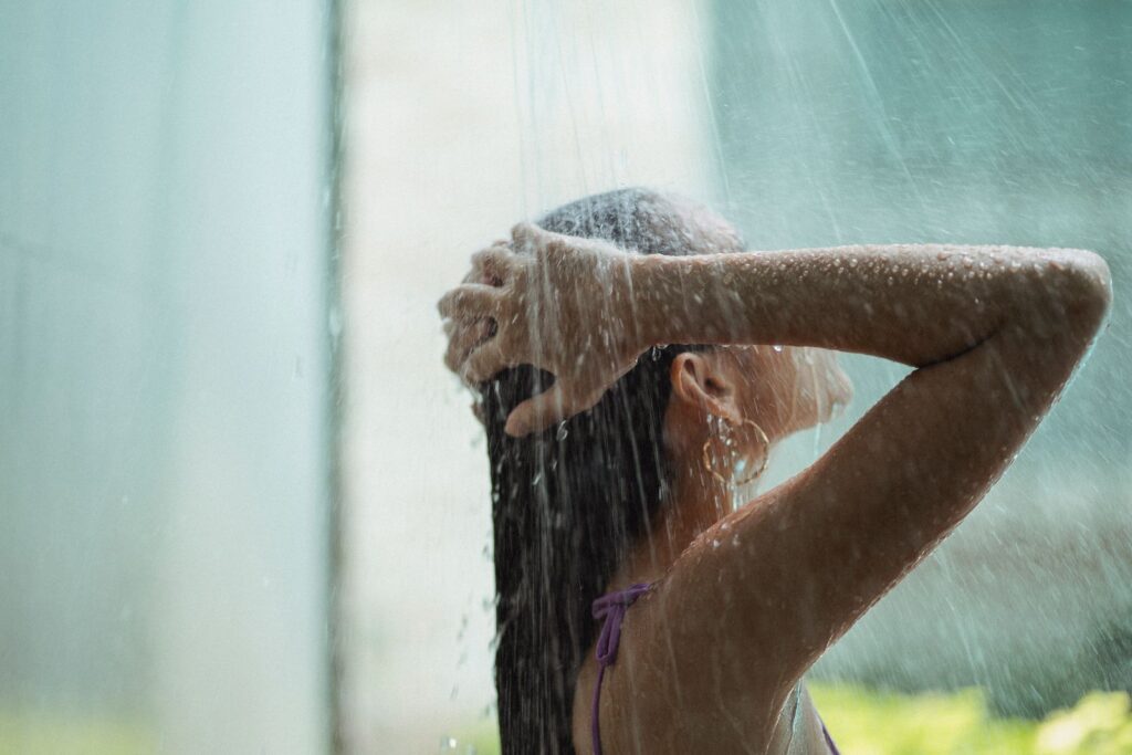 Side view of anonymous young woman with dark hair washing in garden shower on blurred background