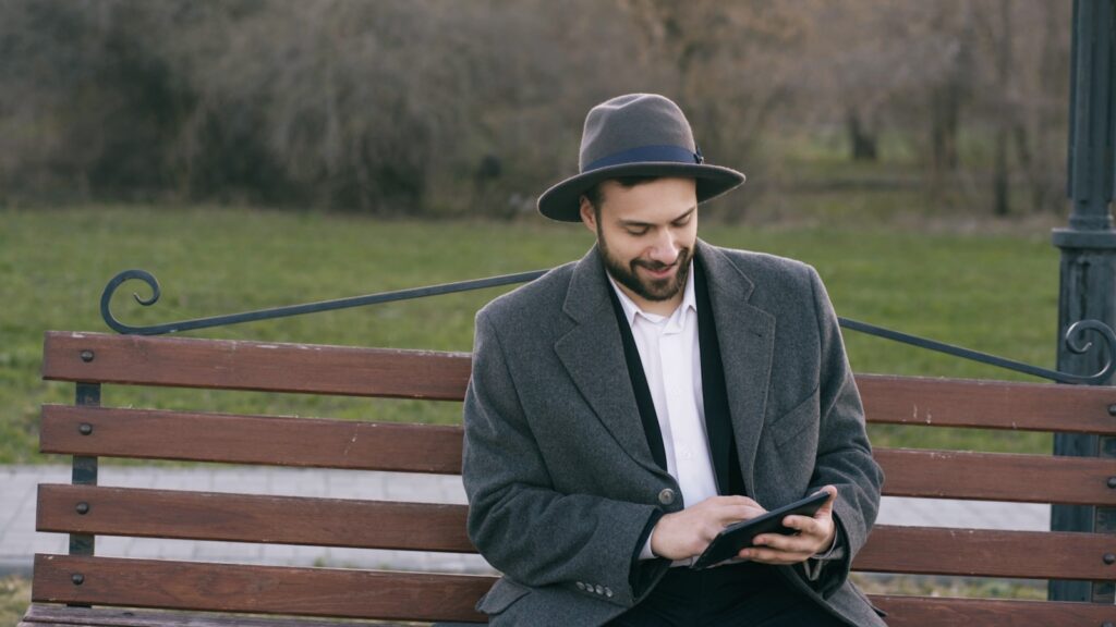 Man in hat using tablet on park bench