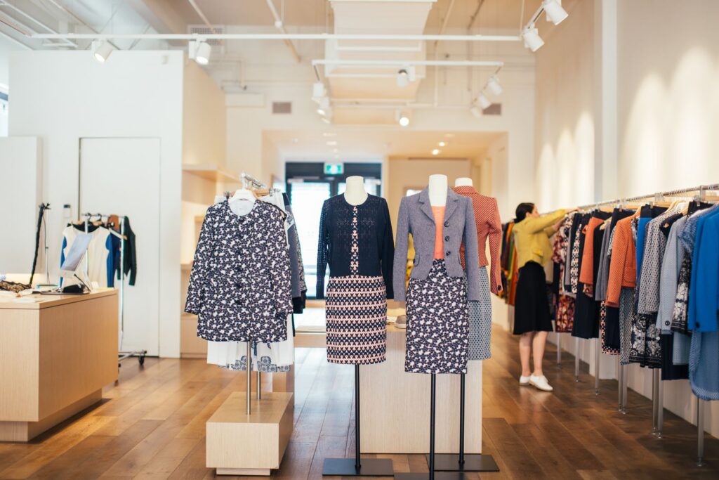 Side view of unrecognizable female seller standing and adjusting stylish colorful clothes hanging on rail in boutique in daytime