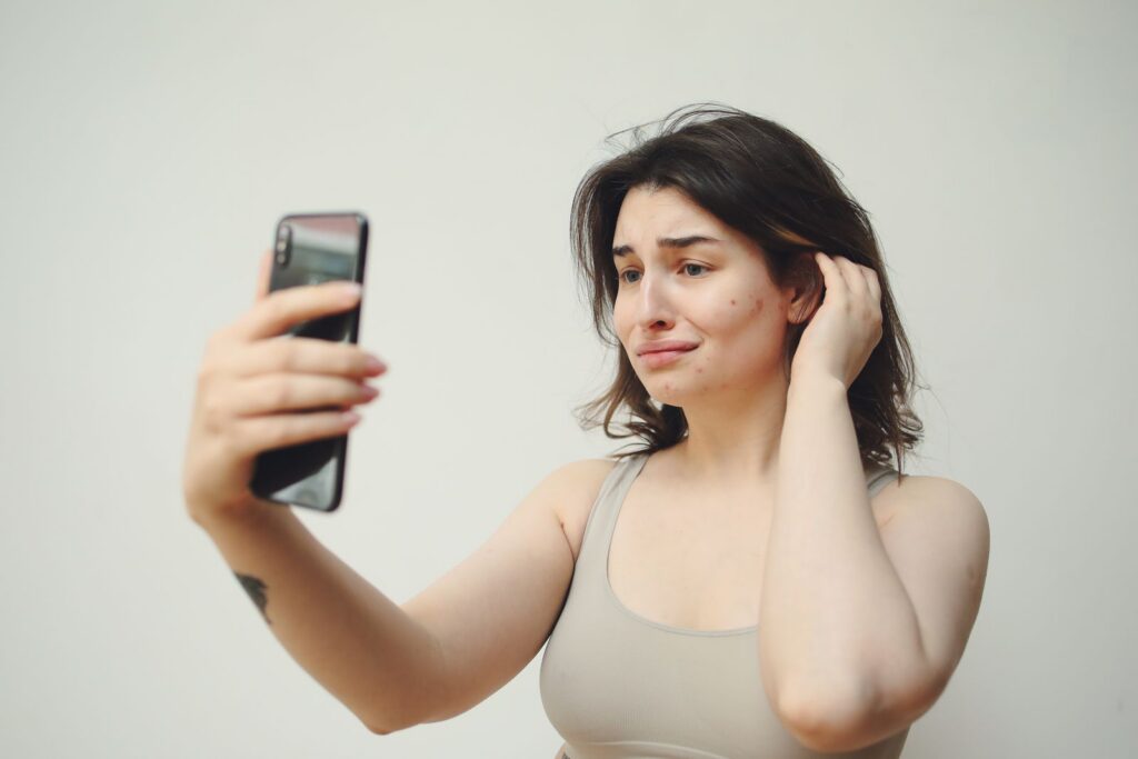 A young woman in a tank top taking a selfie with a worried expression on her face.