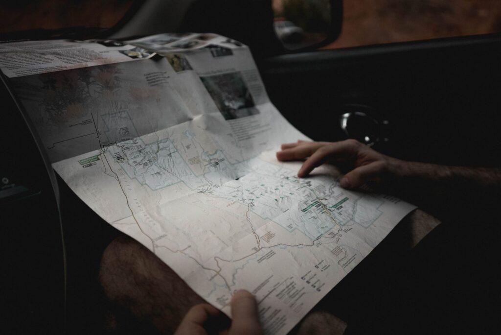 Crop faceless male tourist holding paper map and searching route while sitting in car during trip