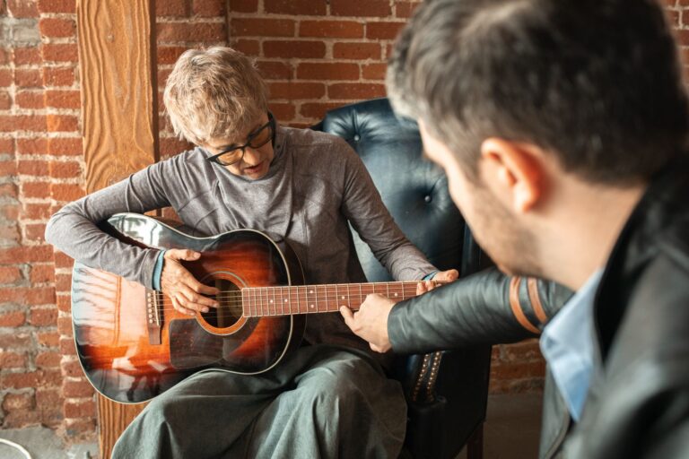 An adult receiving guitar lessons from a tutor in a cozy indoor setting.