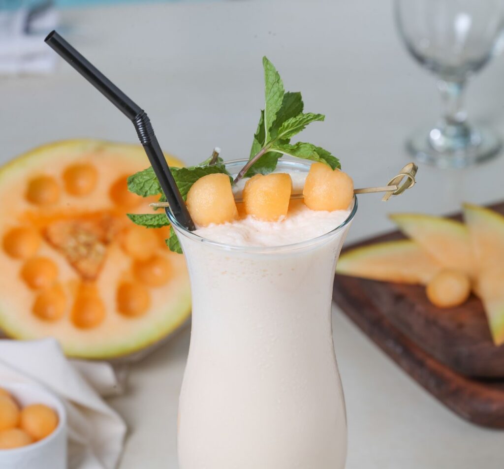 Creamy melon milkshake garnished with mint leaves and melon balls for a refreshing summer drink.
