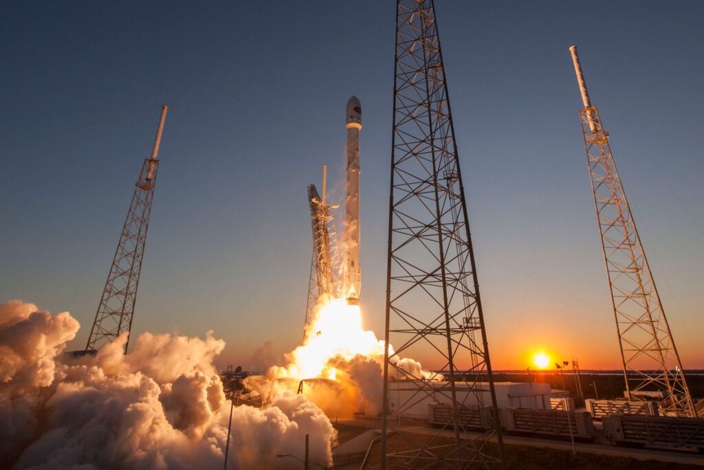 Low angle of modern rocket taking off into cloudless sky during beautiful sunset over space factory
