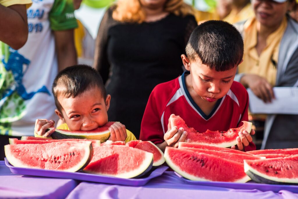 Two boys delightfully eating watermelon slices at a sunny outdoor gathering.