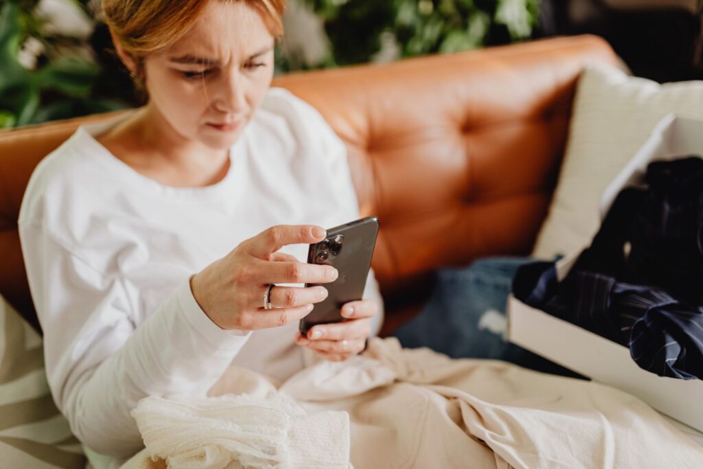 Woman in casual wear using smartphone while sitting on a couch indoors.