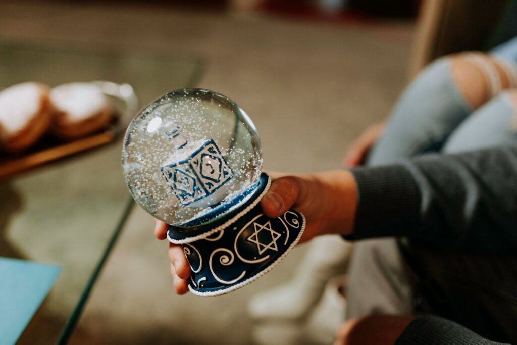 A hand holds a Hanukkah snow globe featuring a dreidel and Star of David symbol.