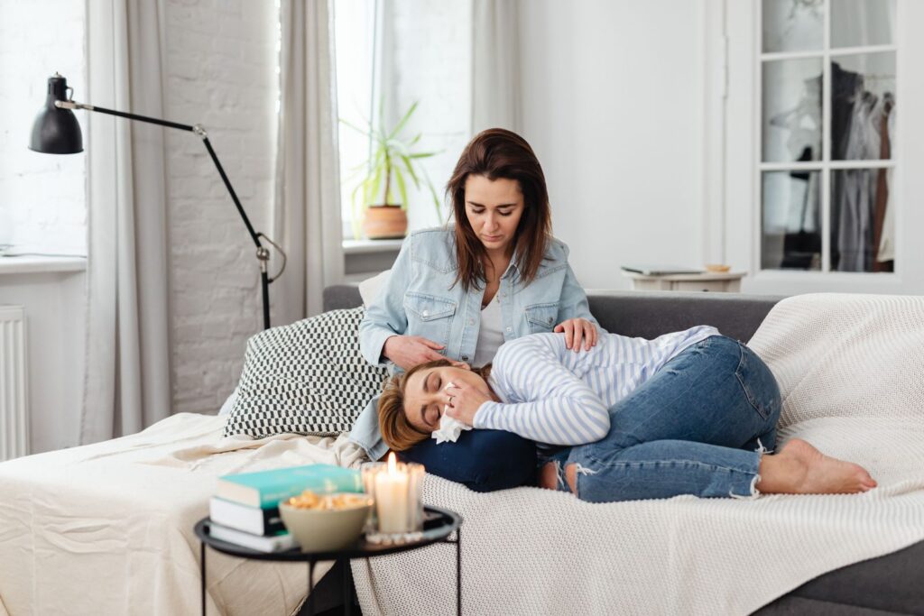 Two women sitting on a couch, with one comforting the other in an emotional moment.