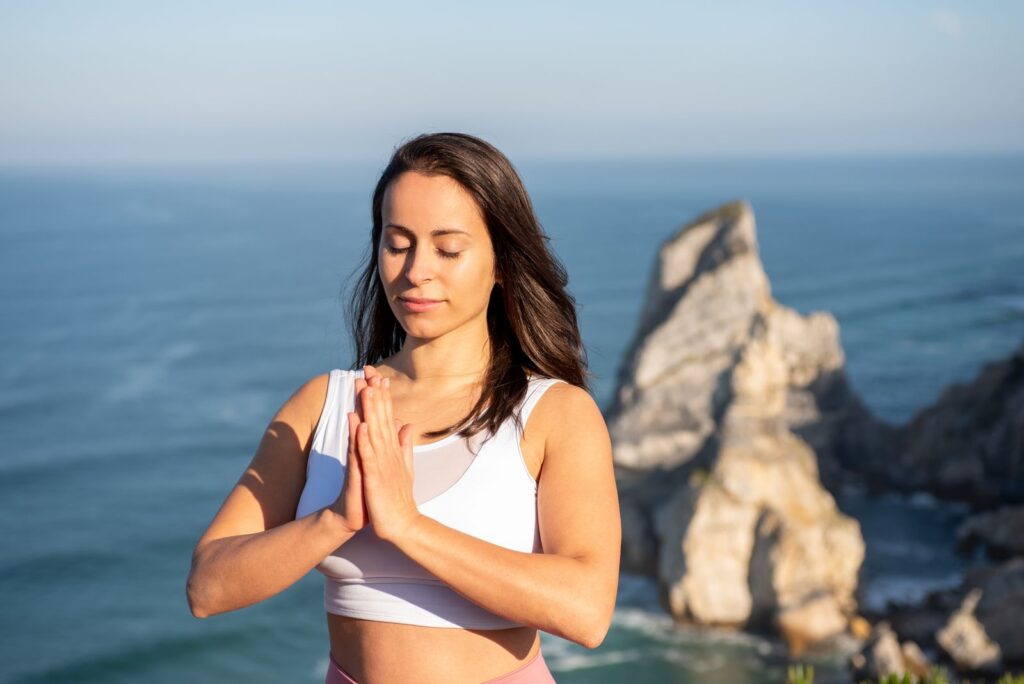 Woman meditating outdoors by the ocean in Portugal, promoting relaxation and mindfulness.