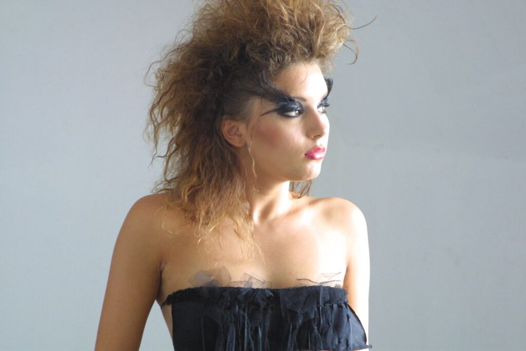 Striking portrait of a woman with dramatic makeup and voluminous hairstyle wearing a black dress.
