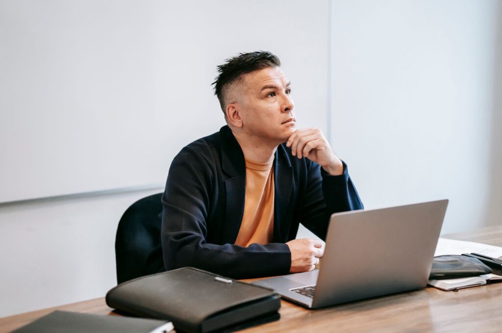 Thoughtful man working on a laptop in an office setting, engaged in remote work.