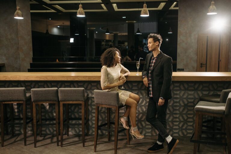 Two young adults enjoying a casual conversation at a sleek, modern bar with elegant lighting.