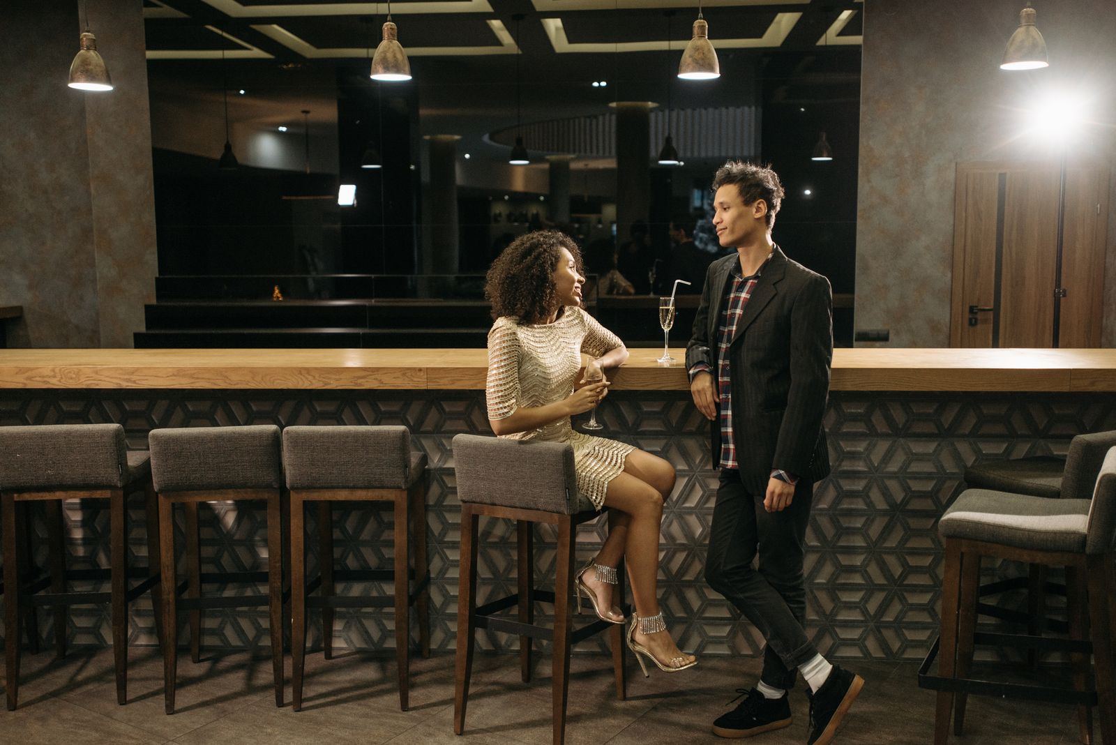 Two young adults enjoying a casual conversation at a sleek, modern bar with elegant lighting.