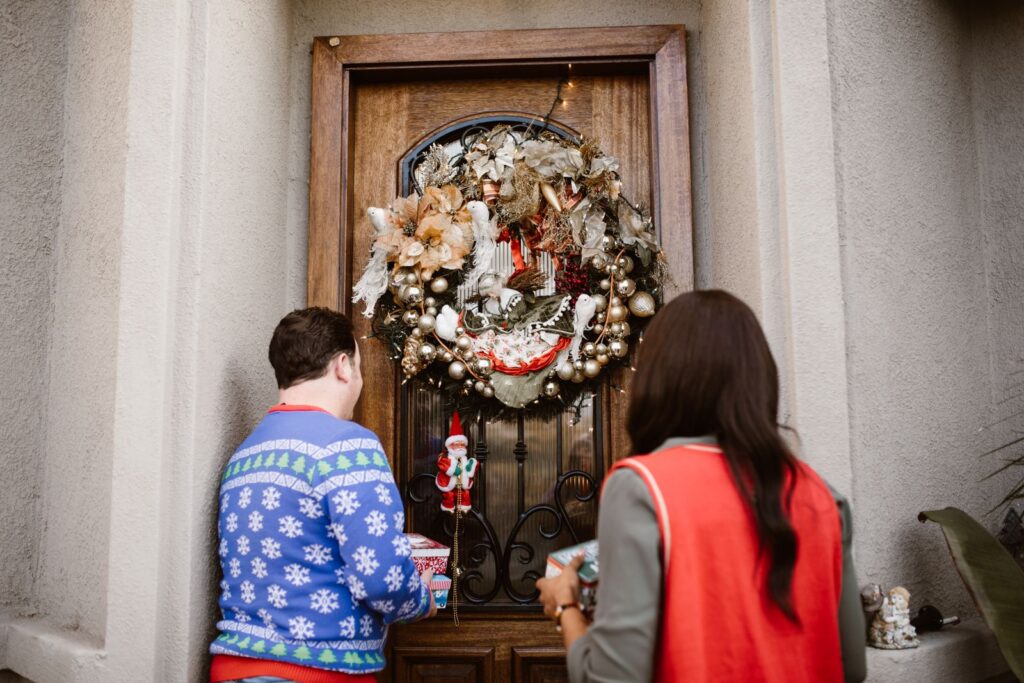 Two adults at a decorated door with wreaths and gifts during Christmas.