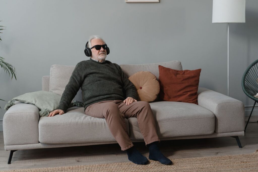 Senior man with headphones and sunglasses relaxing on a sofa indoors.