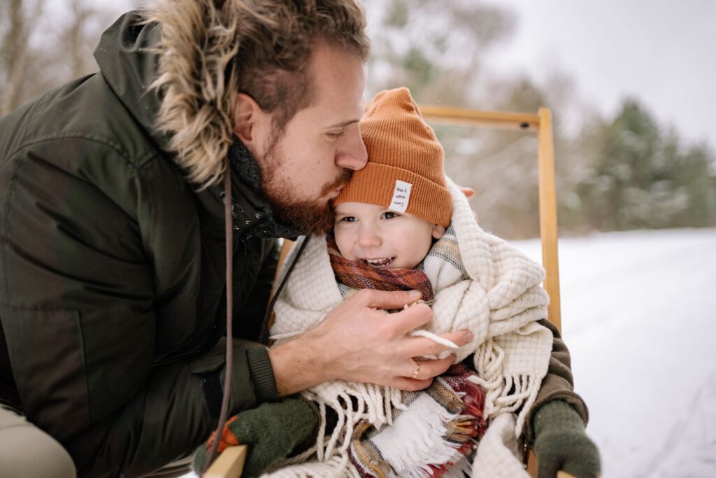 A father lovingly embraces his child in a snowy setting, showcasing warmth and affection.
