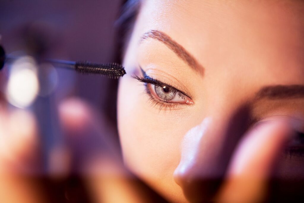 Detailed close-up of a woman applying mascara with focus on her eye.