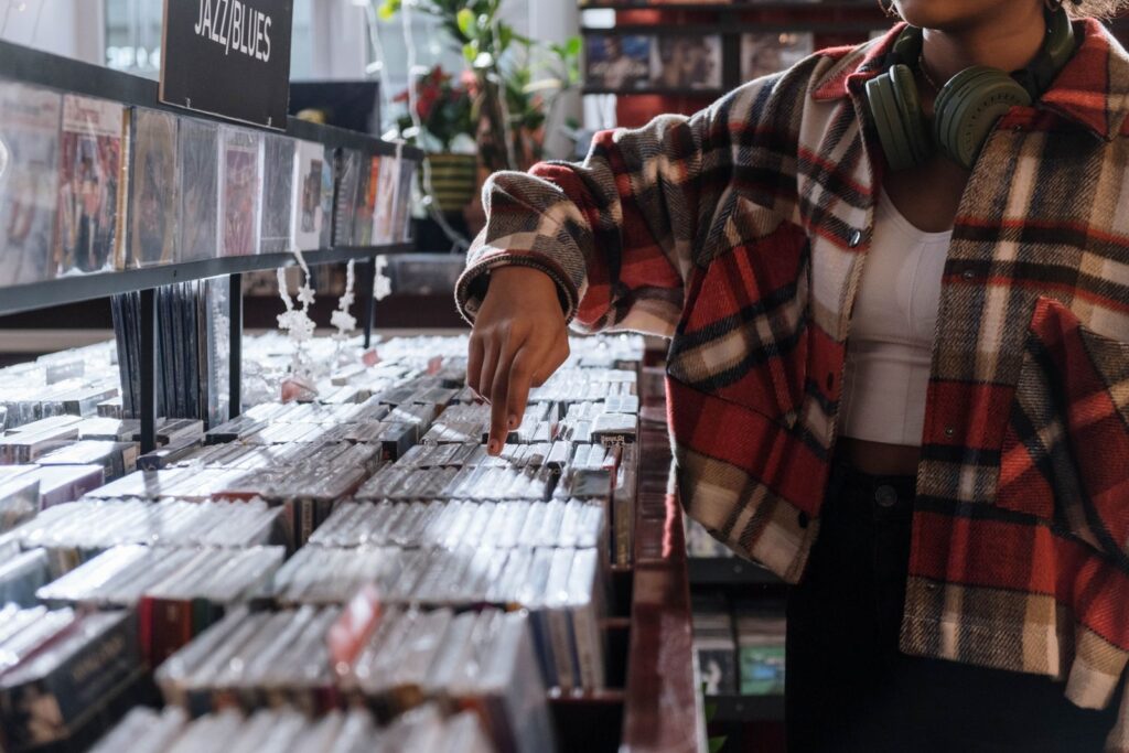 Person browsing through CDs in a music store wearing a plaid shirt and headphones.