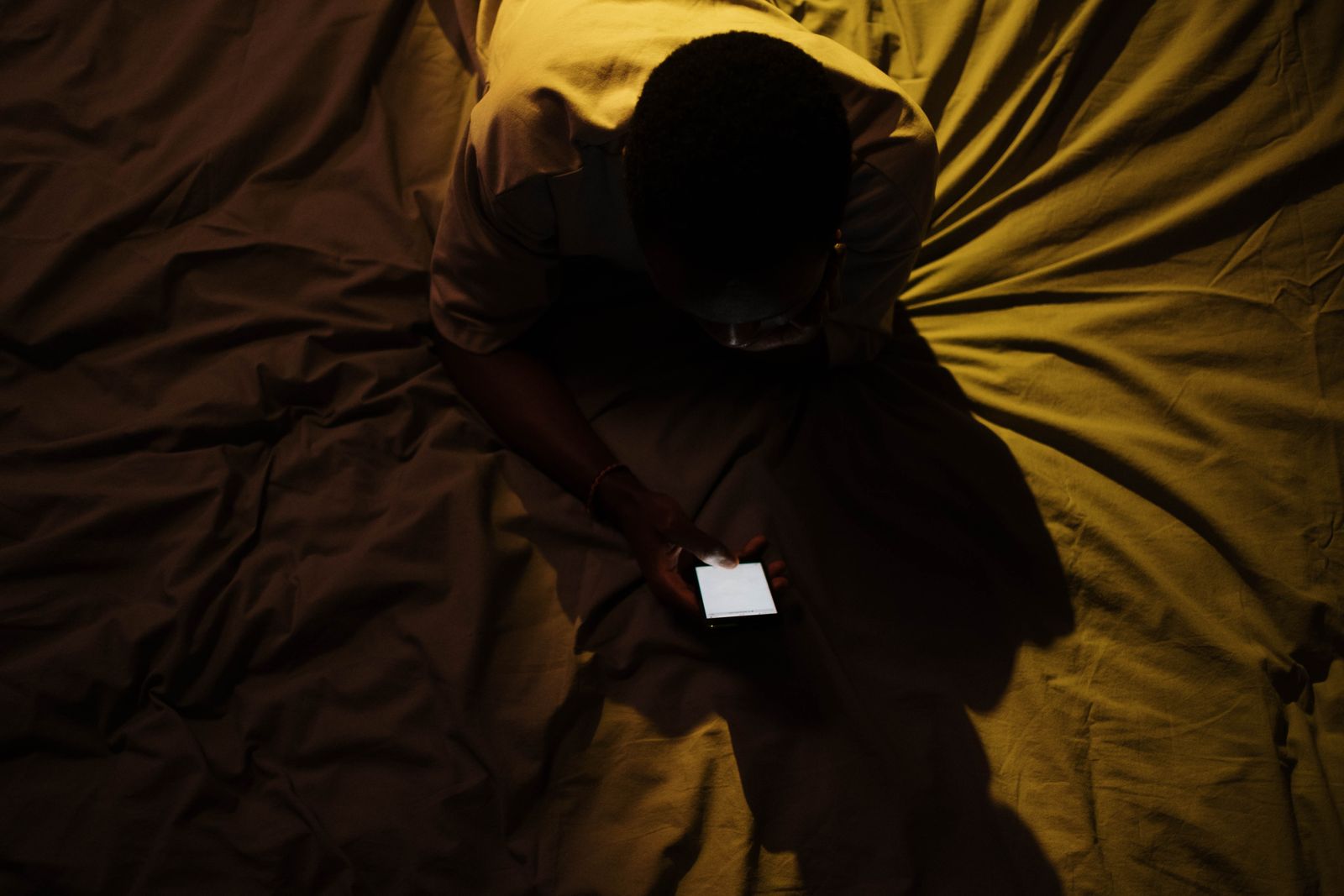 Overhead shot of a person using a smartphone on a bed, creating a moody atmosphere.