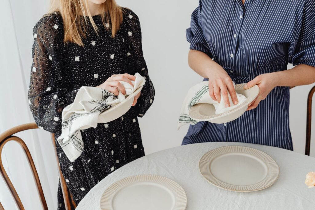 Women drying ceramic bowls and setting a table with plates and napkins.