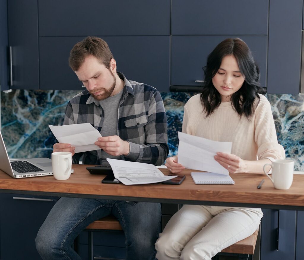 A couple reviewing financial documents at home, showcasing concern and focused collaboration.