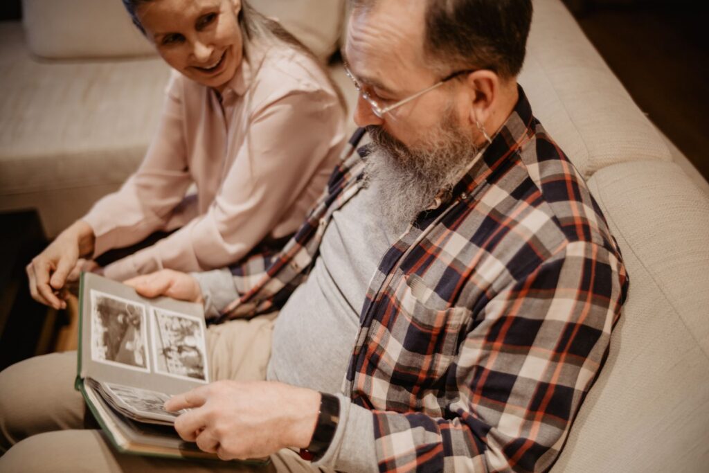 An elderly couple reminiscing with a photo album on a comfortable sofa indoors.