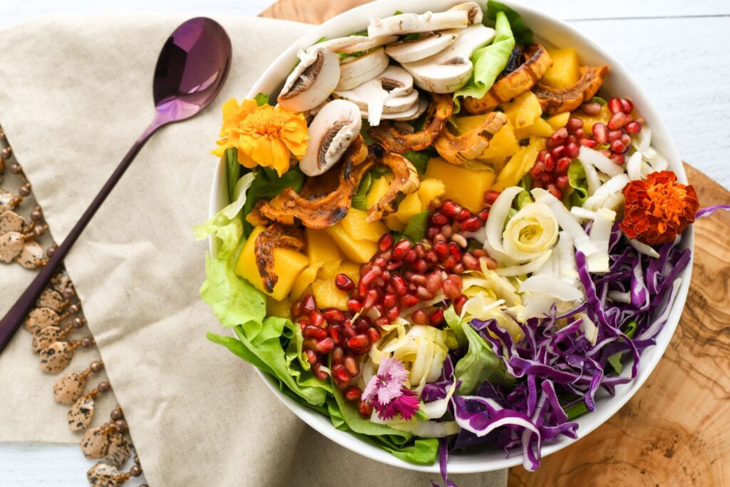 Colorful salad with fresh vegetables and fruits including pomegranate and mango, elegantly plated.