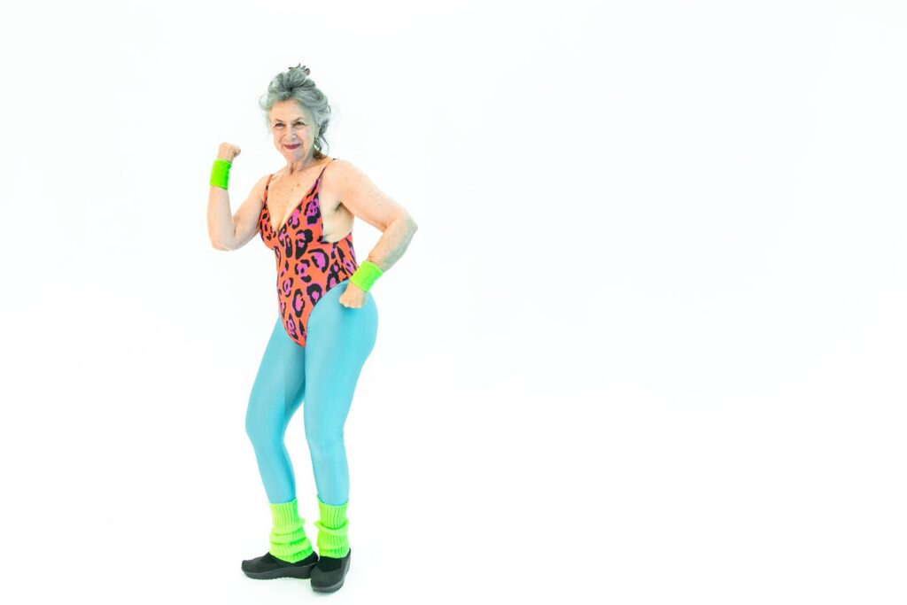 A lively senior woman flexing muscles in colorful retro fitness attire, exuding energy and joy.