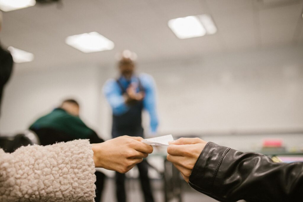 Focused hands exchanging paper in a classroom environment indicating discreet communication.