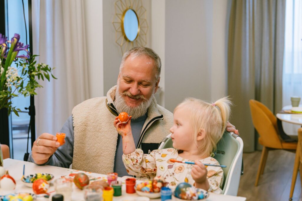 A grandfather and child happily painting Easter eggs together at home, fostering family bonding.