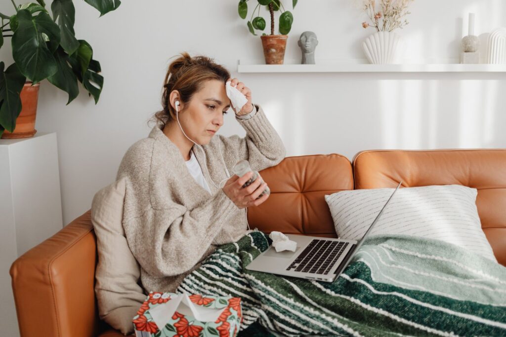 Woman feeling unwell, sitting on a sofa with a laptop and tissue box, indoors