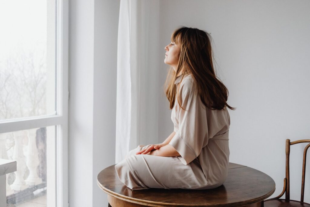 Contemplative woman sitting by a window in a minimalist white room. Perfect for themes of introspection.