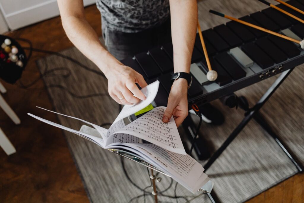 A musician turns pages of sheet music next to a xylophone, focused on musical composition.