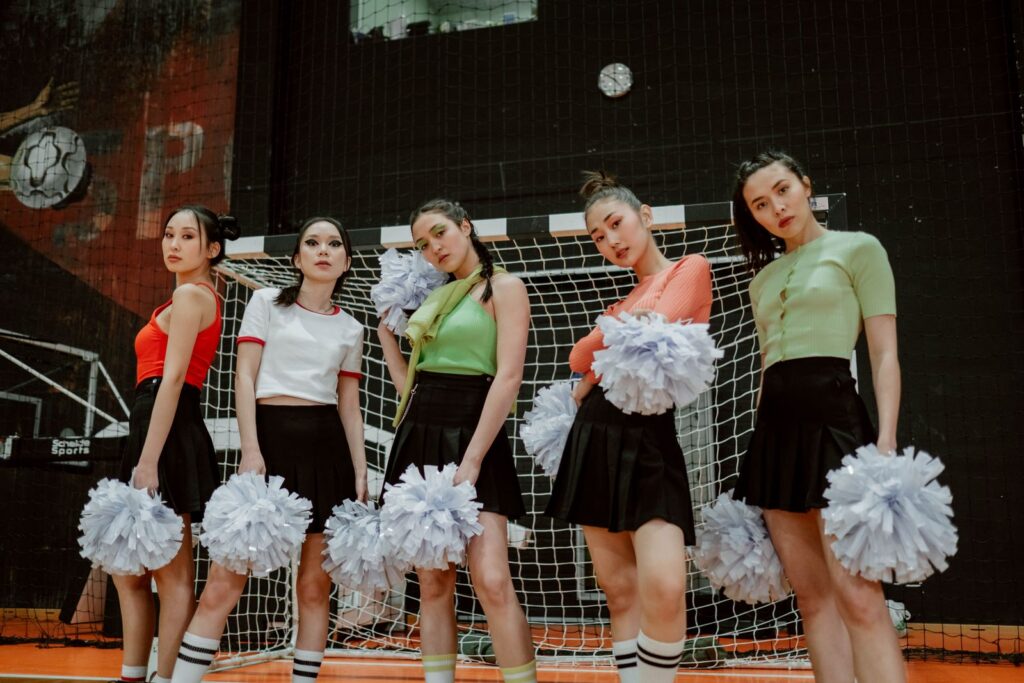 A spirited group of cheerleaders posing indoors with pom poms in a sports hall.