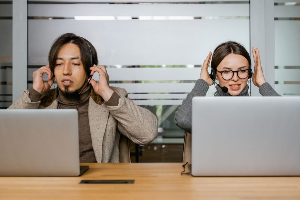 Two customer support agents using laptops and headsets in modern office.