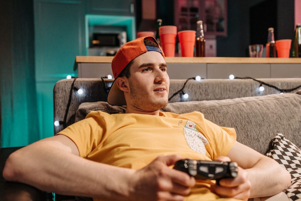 Adult man wearing a yellow shirt and cap, intensely gaming on a couch with a controller.
