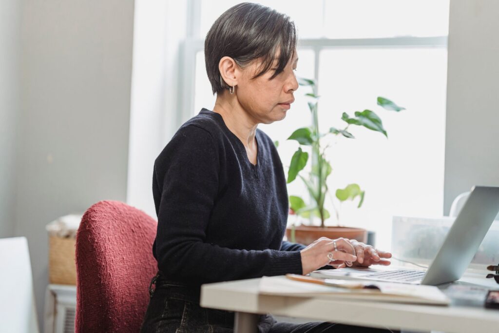 Adult woman focused on laptop work at home office with natural light.