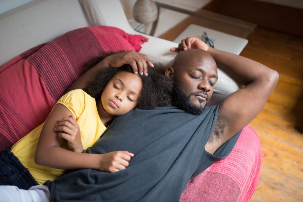 A father and daughter sleeping peacefully on a sofa at home, creating a warm family moment.