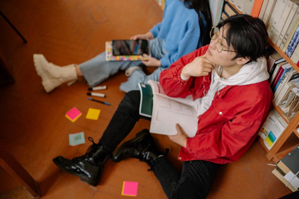 Two students sitting on a library floor, immersed in study with open books and tablets.