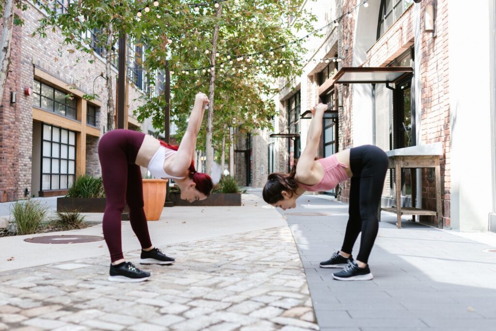 Two women performing flexibility exercises outdoors in an urban street setting.