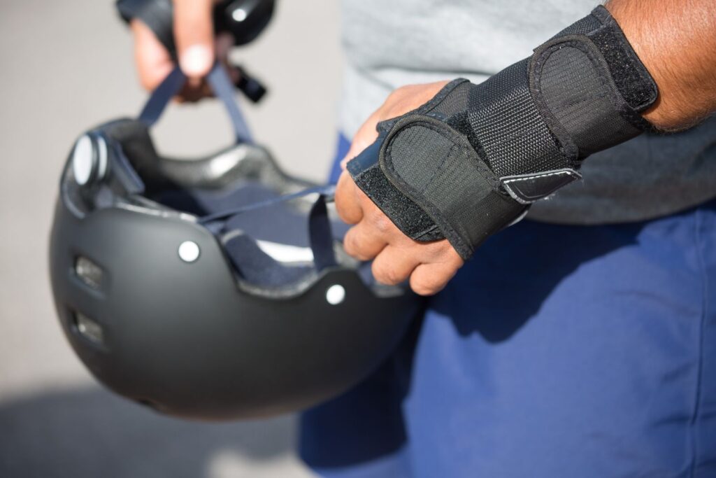 Detailed view of hands handling a helmet and wearing protective gear outdoors.