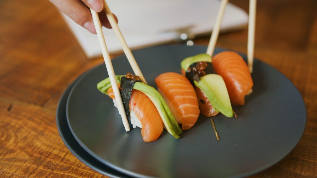 Close-up of salmon nigiri sushi with avocado, presented on a dark plate.