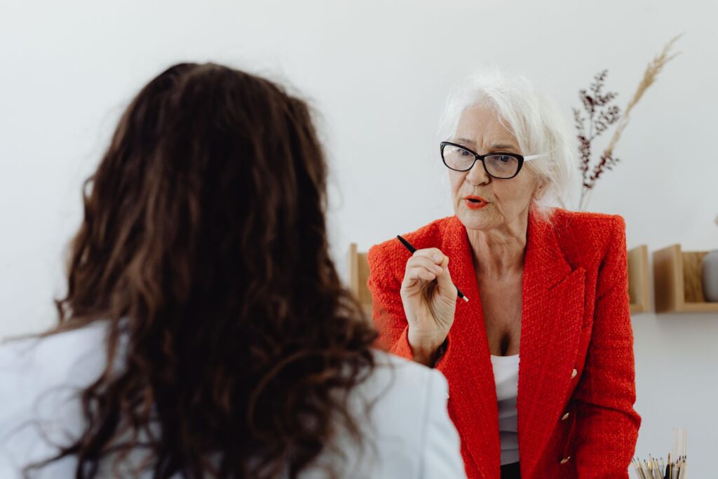 Confident senior businesswoman in red blazer discussing with a colleague in an office setting.